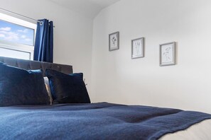 Una camera da letto con un letto, una finestra con tende e tre quadri appesi al muro.
