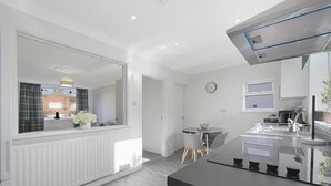 Een moderne keuken met een centraal eiland, een eethoek met een ronde tafel, en uitzicht buiten door een groot raam.