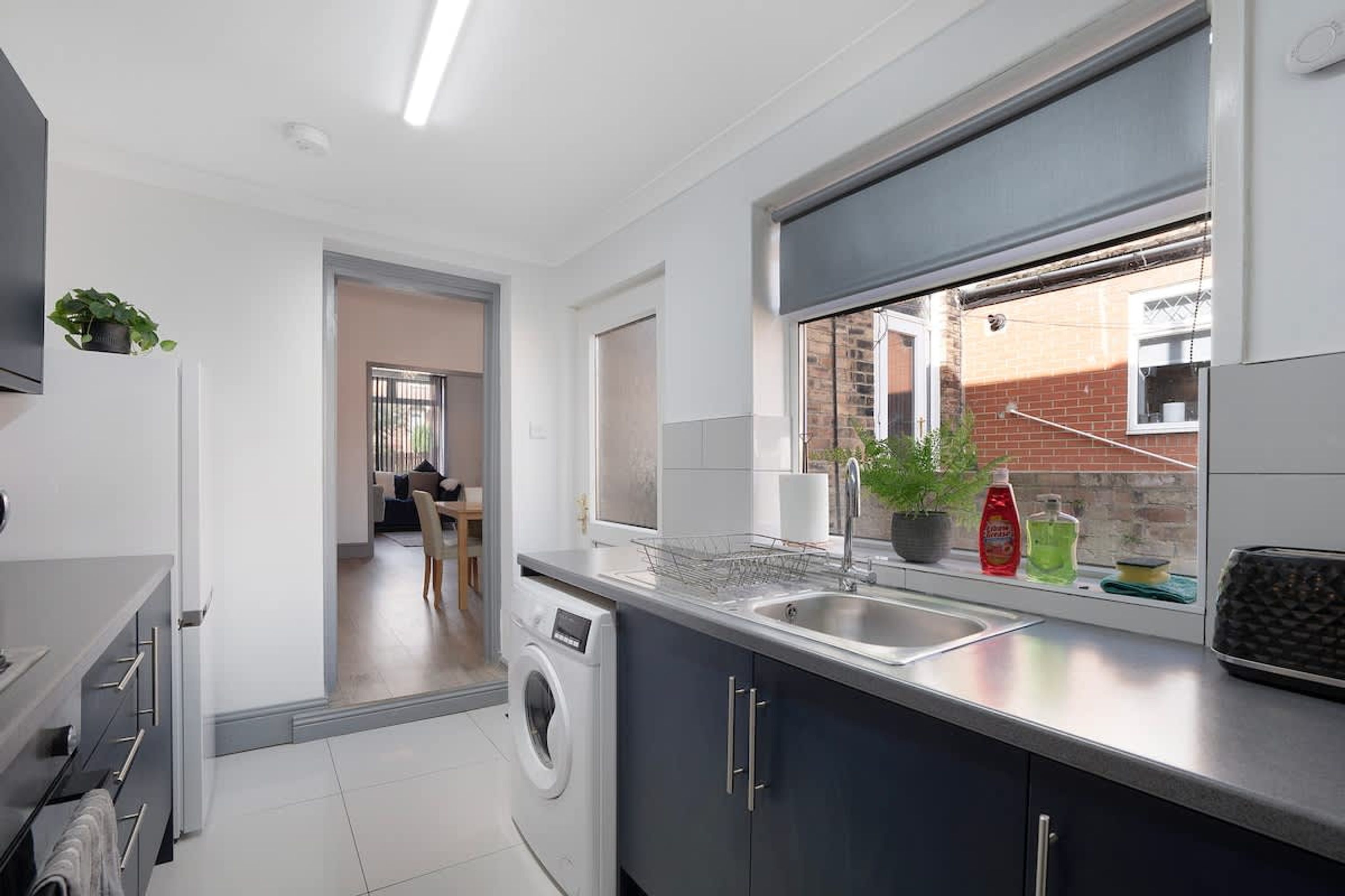 Una cocina moderna con lavadora incorporada, una ventana con vistas a la calle y una zona de comedor al fondo.