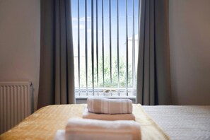 Habitación de hotel con cama, radiador y ventana con persianas verticales.