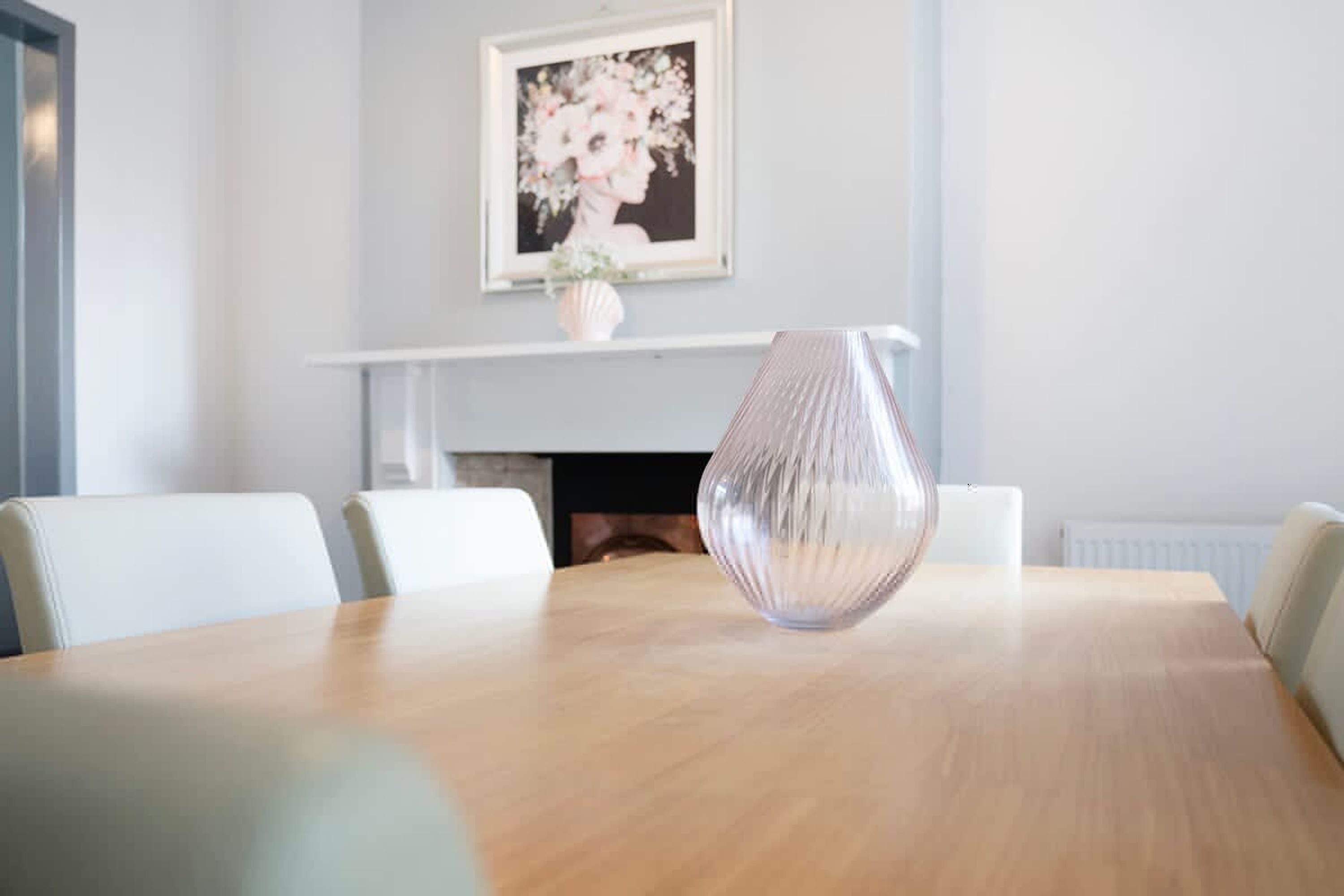 Un salón de conferencias con una mesa de madera, sillas blancas, un jarrón y una obra de arte enmarcada en la pared.