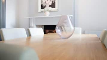 Un salón de conferencias con una mesa de madera, sillas blancas, un jarrón y una obra de arte enmarcada en la pared.