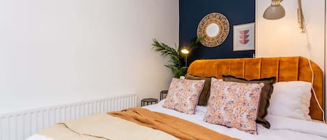 Un dormitorio con cama, lámpara de noche, espejo en la pared y una planta en maceta.