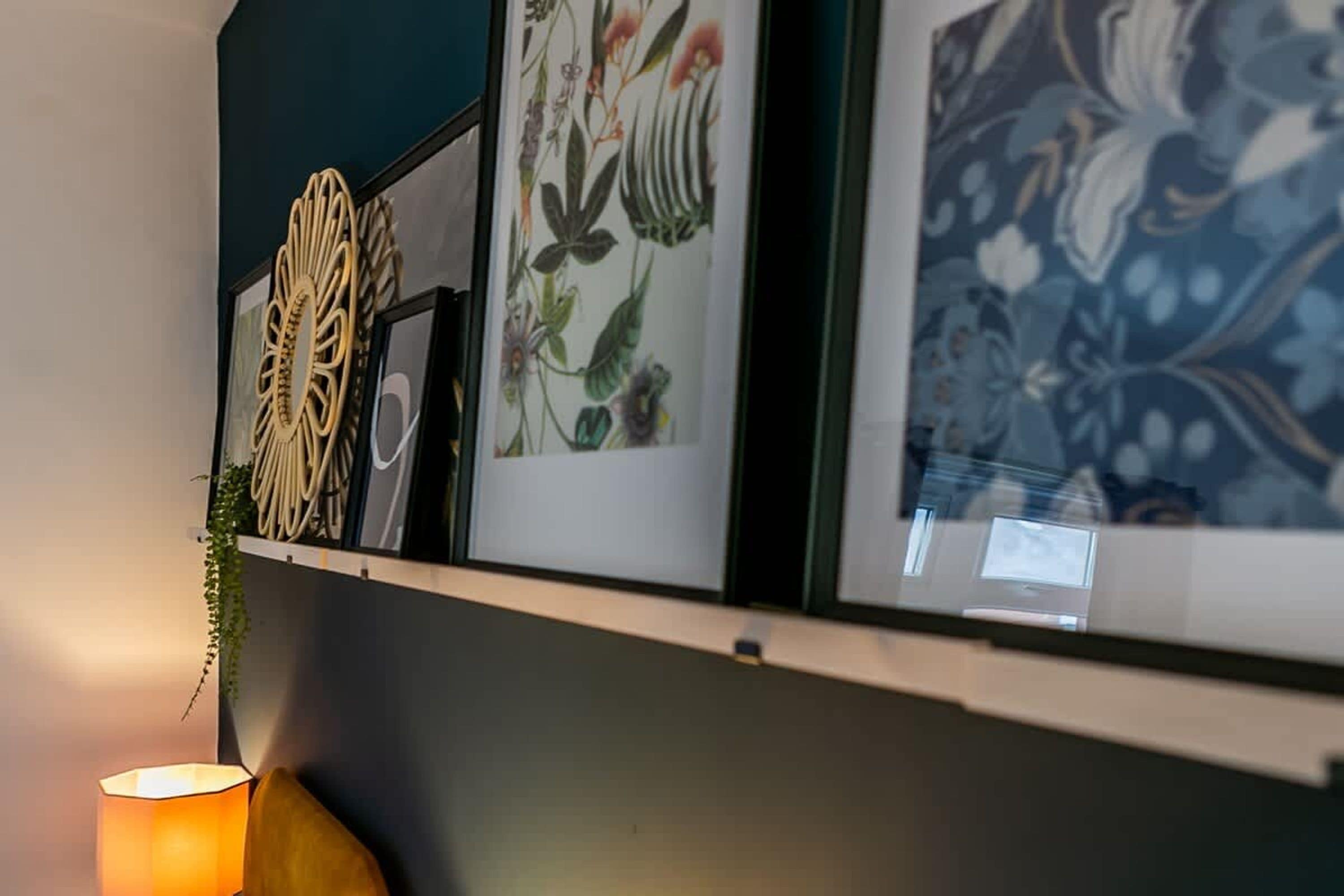 A wall with a shelf displaying framed artwork and a lamp.