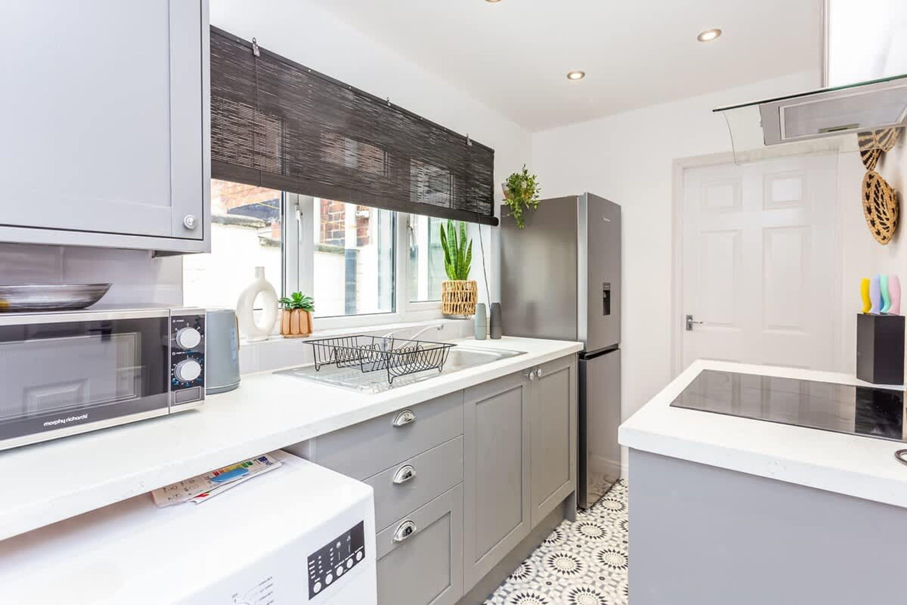 A modern kitchen with grey cabinets, a microwave, a refrigerator, and a window with a view.