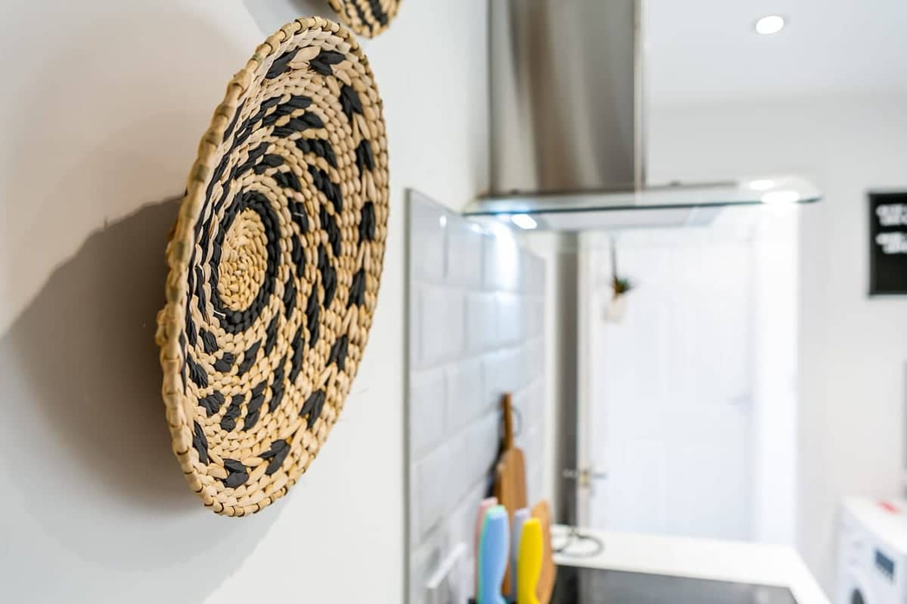 A woven wall hanging in a bathroom with a white tiled wall and a glass shower enclosure.