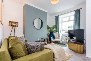 A modern living room with a sofa, a TV, a round mirror, and a lamp. - Two Bedroom Family Apartment Near Town Centre Chic Stay (Darlington)