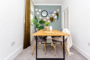 A dining area with a wooden table, two chairs, a potted plant, and a wall decorated with various plates and a clock. - Two Bedroom Family Apartment Near Town Centre Chic Stay (Darlington)