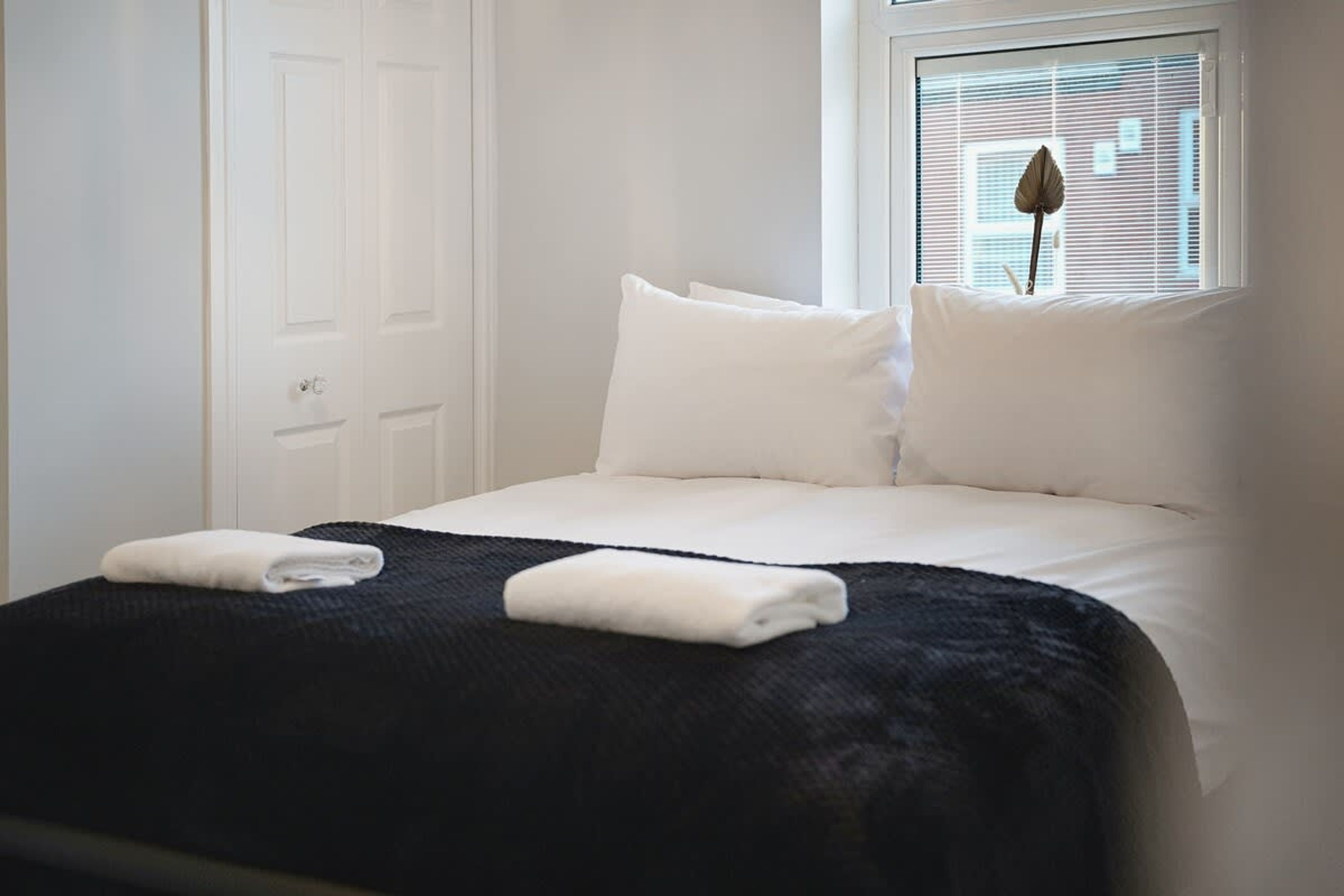 A neatly made bed with white linens and a dark-colored throw blanket.