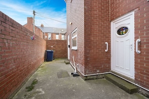 A narrow alleyway with a brick wall on one side and a white door on the other. - Chic 2 Bed With Wifi Parking Ideal for Work Stay (South Shields)