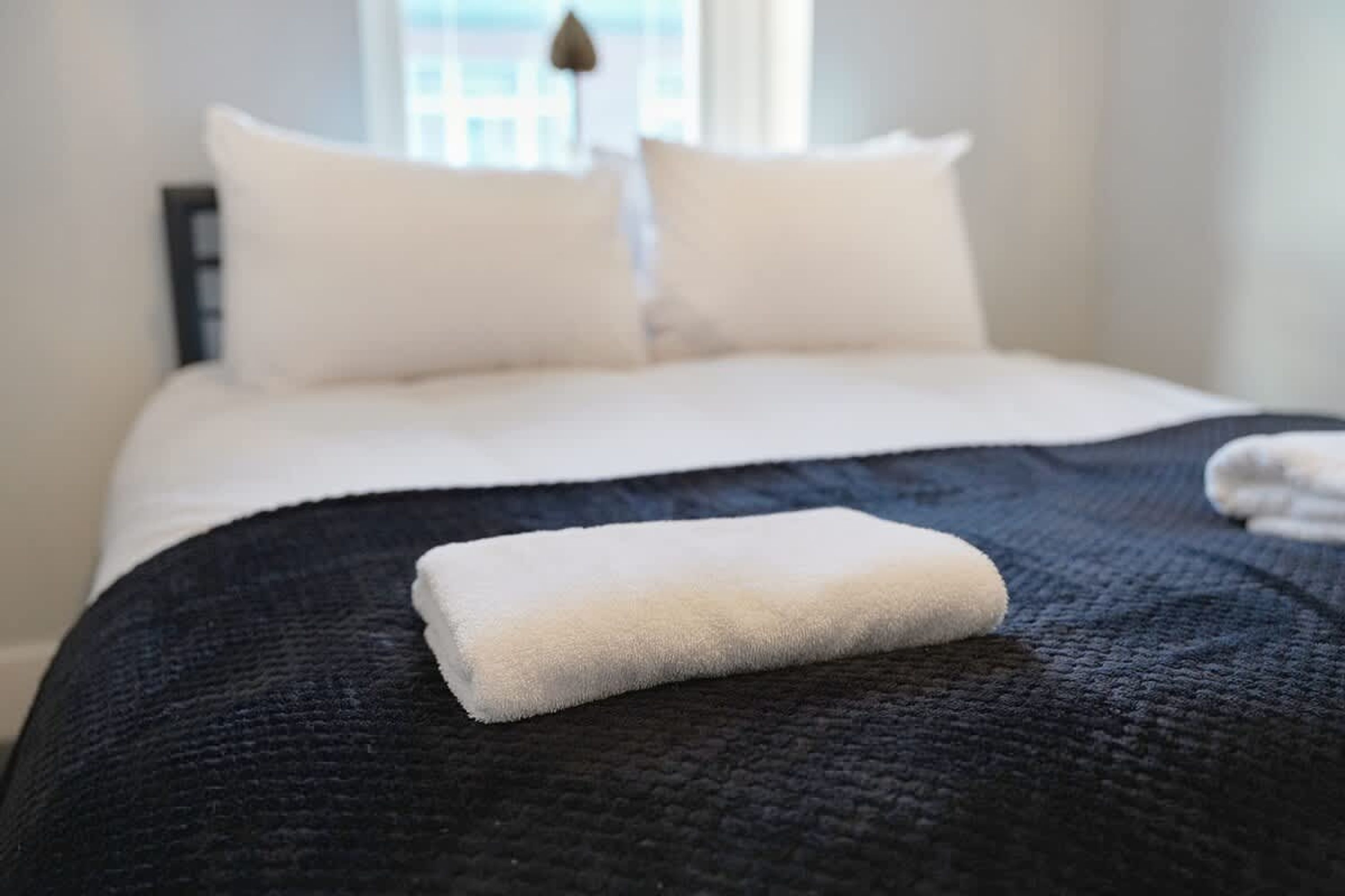 Un lit bien fait, recouvert d’une couvre-lit de couleur sombre et agrémenté de deux oreillers blancs.