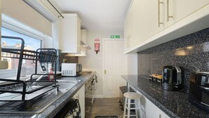 A compact kitchen with a microwave, kettle, and coffee machine. There is a window with a view of buildings outside. - Chic 2 Bed With Wifi Parking Ideal for Work Stay (South Shields)