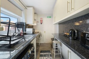 A compact kitchen with a microwave, kettle, and coffee machine. There is a window with a view of buildings outside. - Chic 2 Bed With Wifi Parking Ideal for Work Stay (South Shields)