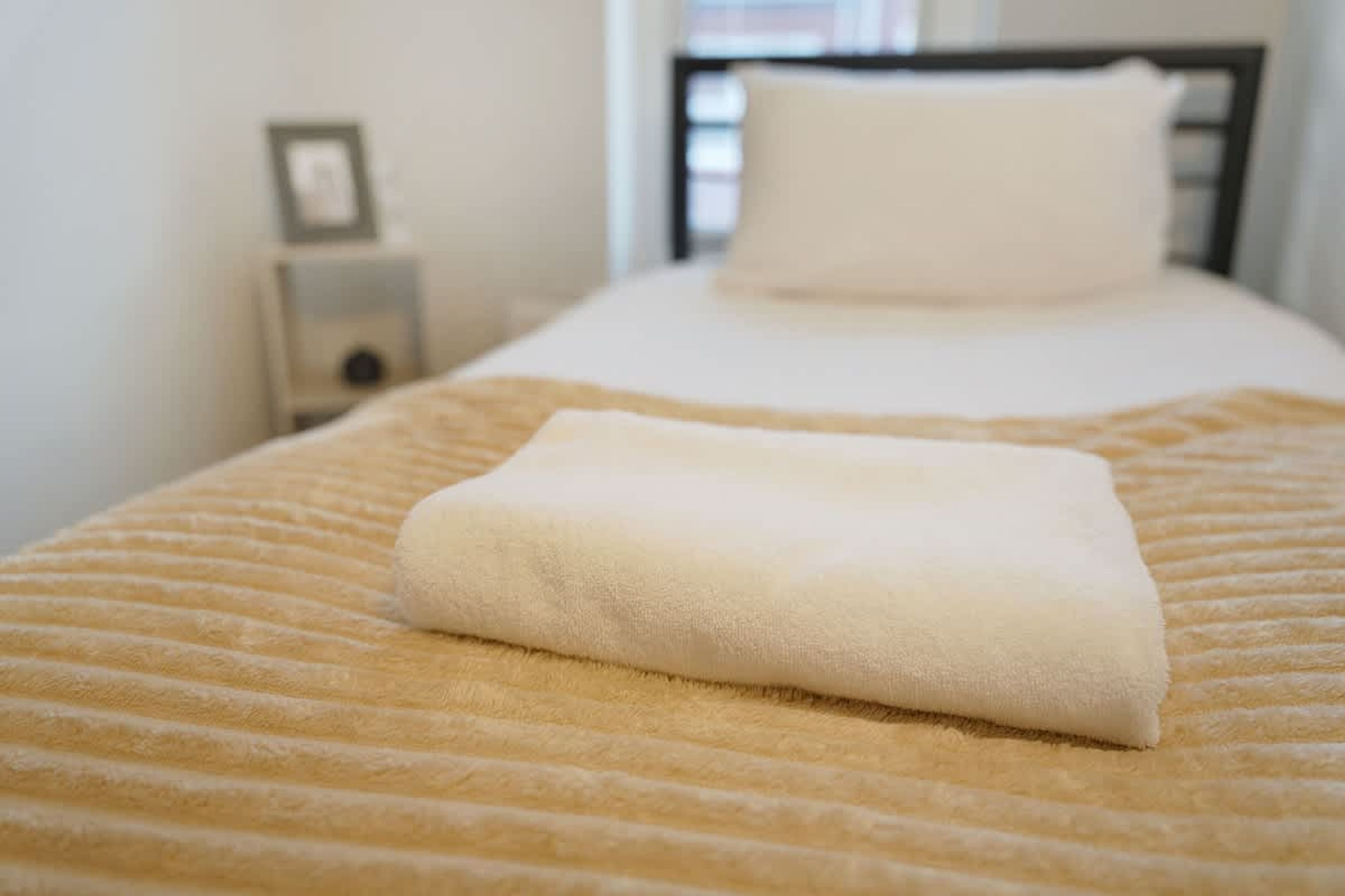 A neatly made bed with a folded white towel on a striped bedspread.