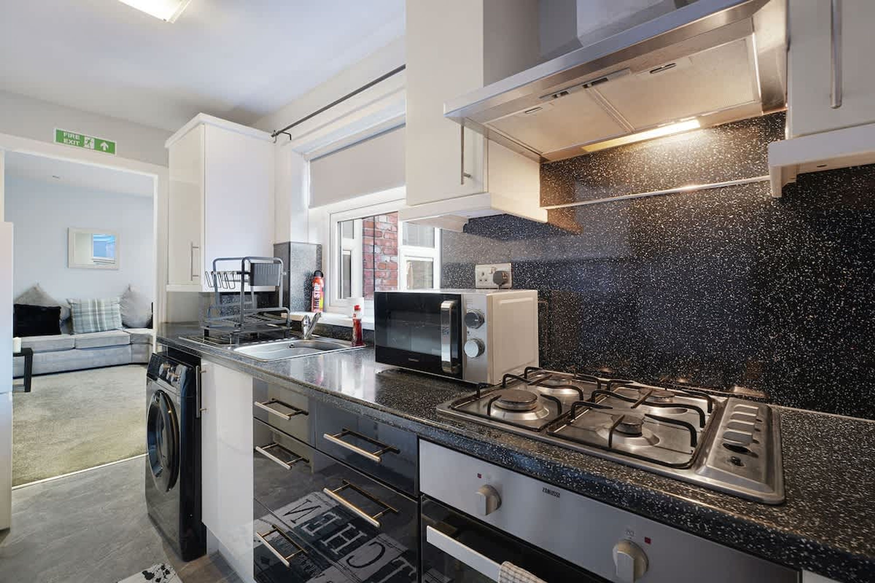 A modern kitchen with a gas stove, microwave, and built-in oven. There is a washing machine and a small dining area with a table and chairs.