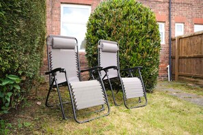 Two outdoor lounge chairs with a metal frame and fabric seat and backrest, positioned on a grassy lawn with a brick wall and a wooden fence in the background. - Modern 3BR Washington Sleeps 6 by Stay With Us (Washington)