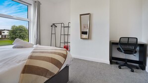 Ein Hotelzimmer mit Bett, Schreibtisch, Stuhl, Spiegel und einem fensterbepflanzten Fenster.