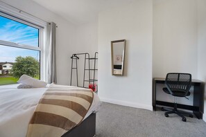 Ein Hotelzimmer mit Bett, Schreibtisch, Stuhl, Spiegel und einem fensterbepflanzten Fenster.