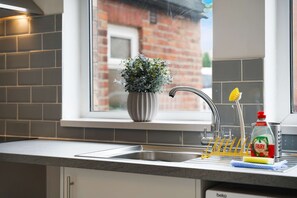 Eine Küche mit einem Edelstahlspülbecken, einem Blumentopf am Fensterbrett und einer Flasche Fairy Spülmittel.