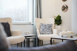 Ein modernes Wohnzimmer mit zwei weißen Sesseln, einem Couchtisch, einem Beistelltisch und einem Blumentopf.