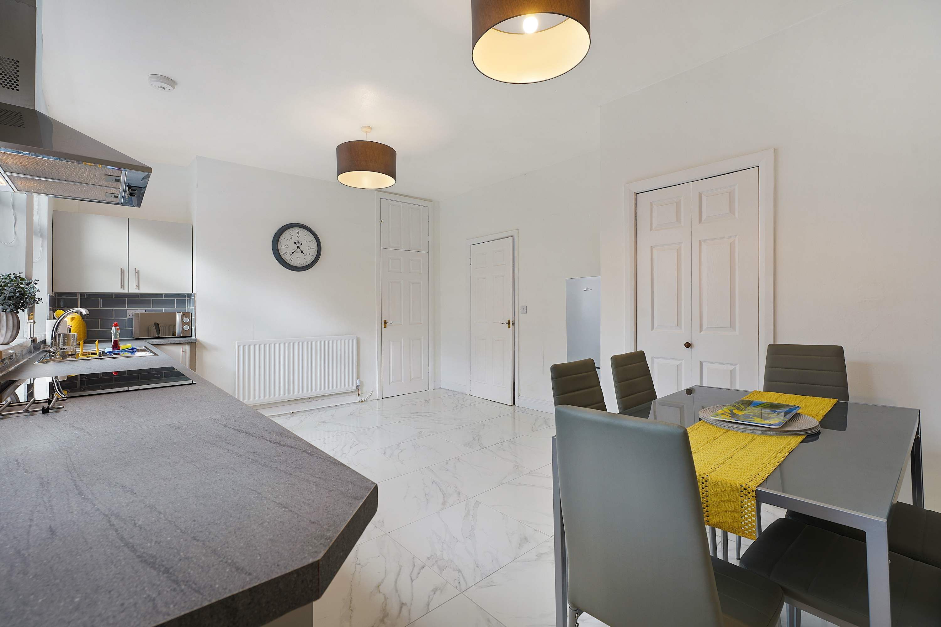 A modern kitchen with a built-in oven, a dining area with a table and chairs, and a white door.