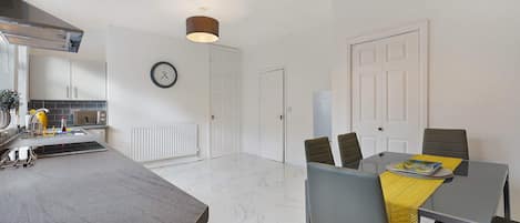 A modern kitchen with a built-in oven, a dining area with a table and chairs, and a white door.