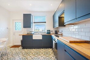 A modern kitchen with a central island, white tiled backsplash, and a window with blinds. - Chic 3BR Rotherham Parking Wifi By Stay With us (Rotherham)