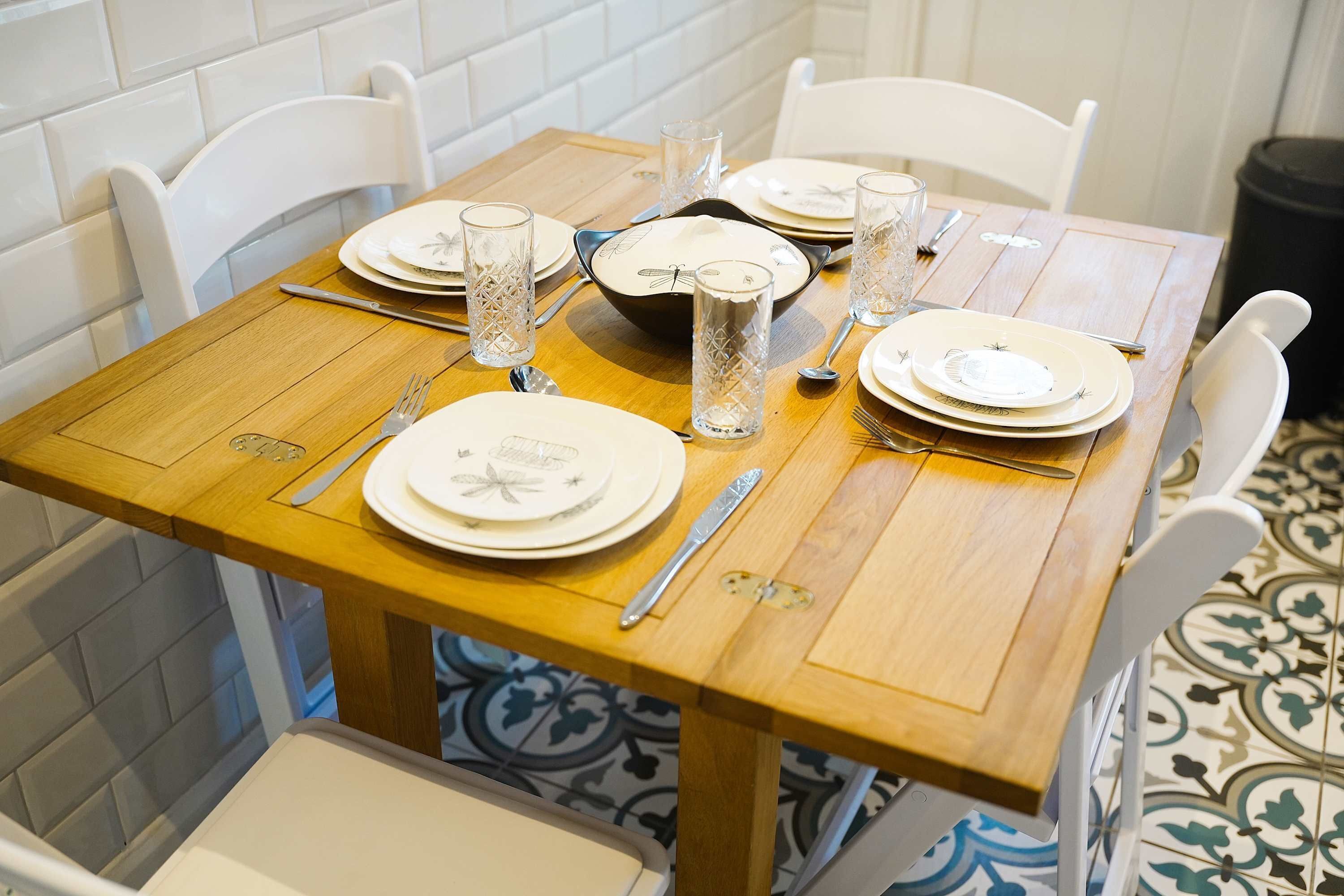 Een eettafel gedekt met borden, glazen, bestek en een kom.