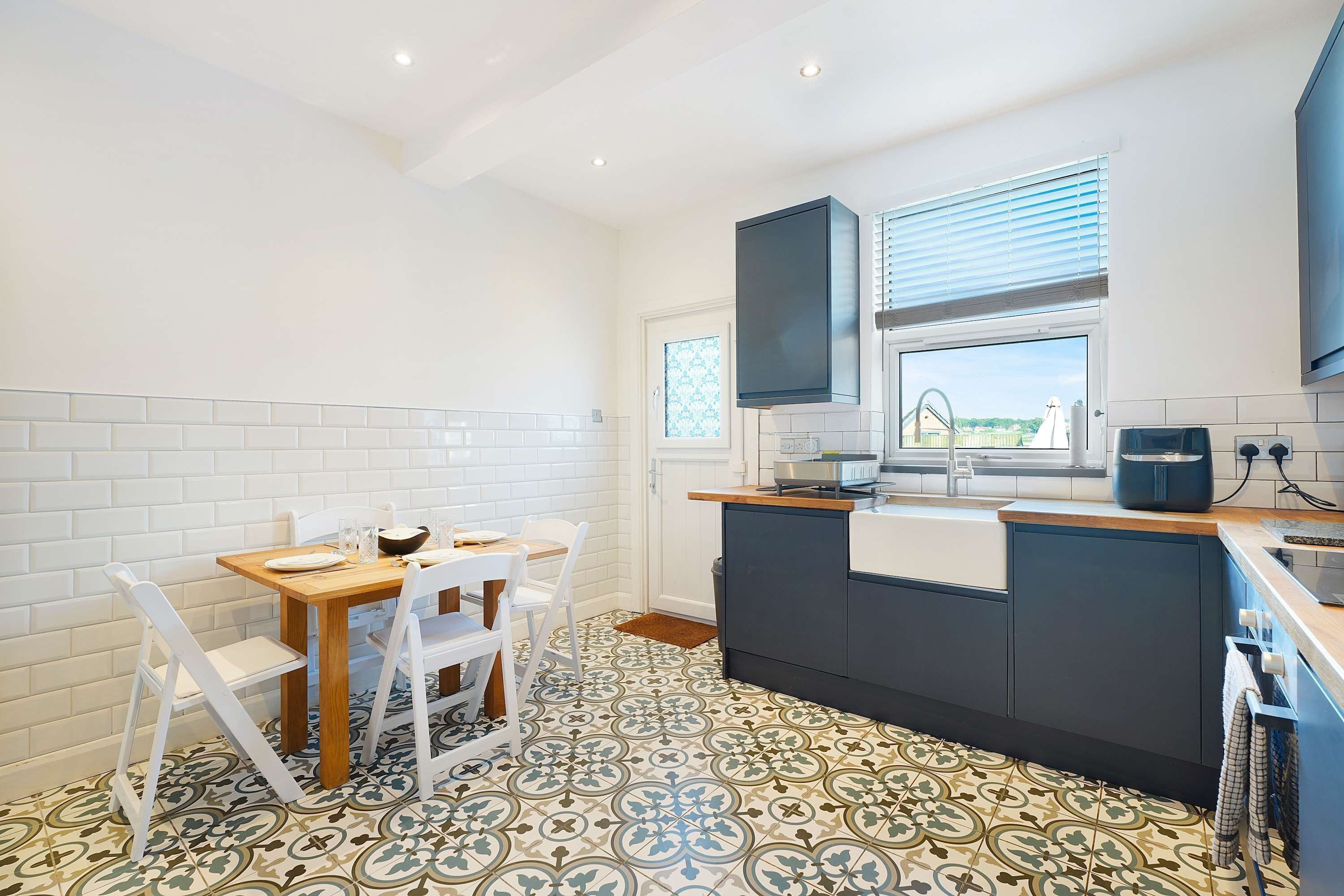 A modern kitchen with white cabinetry, a wooden dining table, and patterned floor tiles.