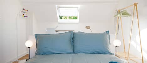 A bedroom with a bed, bedside lamps, a hanging light fixture, a window, and a clothes drying rack.