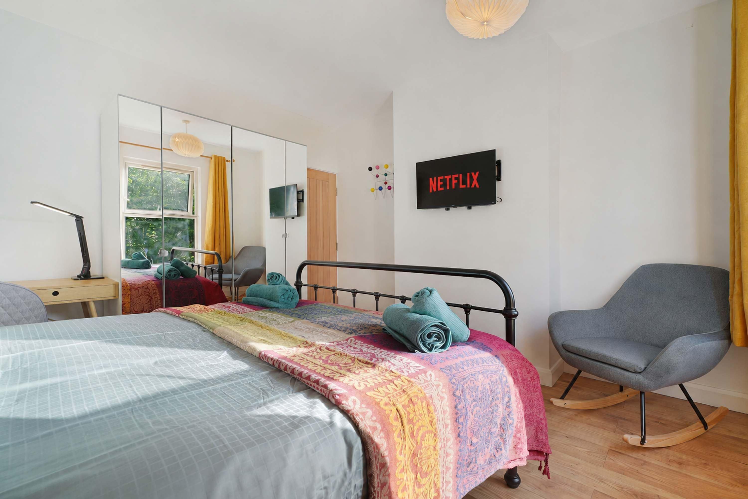 A bedroom with a bed, a desk, a chair, a TV, and a wall-mounted artwork.
