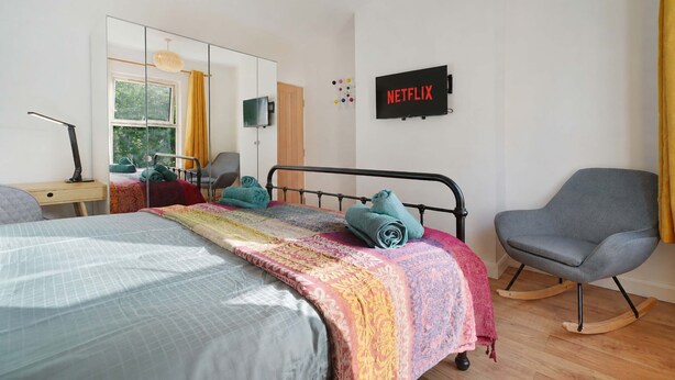 Quarto com cama, escrivaninha, cadeira, televisão e obra de arte na parede.