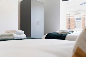 Habitación de hotel con dos camas, un armario y vista a un edificio de ladrillo.