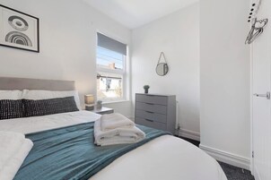 Un dormitorio con cama, cómoda, ventana y espejo adosado a la pared.