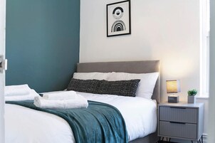 Una cama bien hecha con ropa de cama blanca y aguamarina, cabecera gris y almohada con estampado blanco y negro.