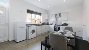 A modern kitchen with a built-in washer, a dining area with a table set for four, and a view of the outside through a window. - Charming 3BR in Blyth (Blyth)