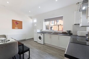 Una cocina moderna con lavadora integrada, un comedor con mesa y sillas, y una ventana que ofrece vista a un edificio de ladrillo.