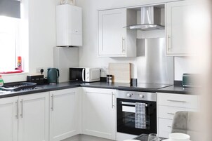 Cocina moderna con armarios blancos, estufa de acero inoxidable, horno empotrado y ventana con un objeto rojo en el alféizar.