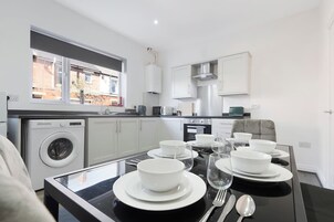 Una cocina moderna con lavadora integrada, una mesa de comedor lista para cuatro personas y vistas a un área residencial a través del ventanal.