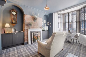 A room with a fireplace, a clock, a chair, and a window with blinds. - Boutique Apartment in Hartlepool With Free Wifi (Hartlepool)