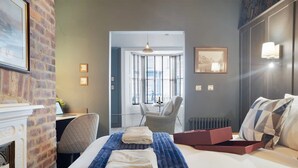 Ett hotellrum med en säng, ett skrivbord, en stol, en öppen spis och utsikt över staden genom fönstret.