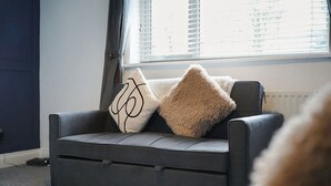 Ein graues Sofa mit zwei Zierkissen vor einem Fenster mit Jalousien.