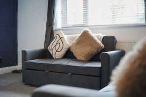 Ein graues Sofa mit zwei Zierkissen vor einem Fenster mit Jalousien.