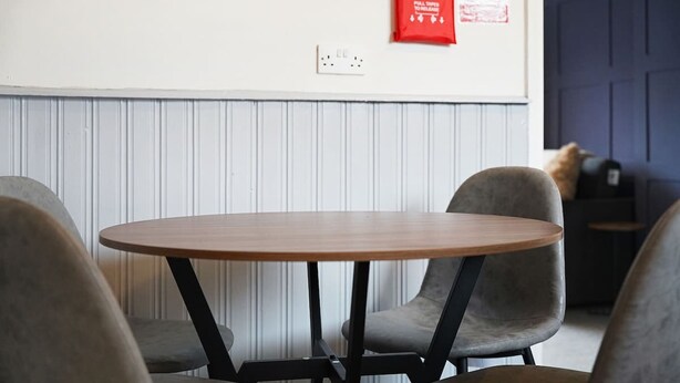 Ein runder Tisch mit vier Stühlen in einem Raum, dessen Wand weiß und die Tür blau ist.