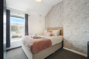 A bedroom with a bed, a window, and a wall with a bird pattern. - Work Friendly 3 Bed House With Sofa Beds Sleeps 7 (Stockton-on-Tees)