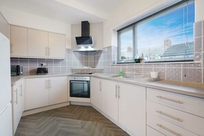 Een keuken met witte kasten, een ingebouwde oven, een magnetron en een raam met zonwering.