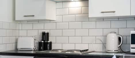 A modern kitchen with white cabinets, a gas stove, a kettle, and a coffee maker.