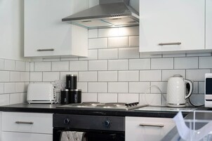 Una cocina moderna con gabinetes blancos, una estufa a gas, un hervidor y una cafetera.
