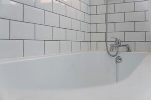 Un baño con paredes de azulejos blancos y una bañera con ducha.