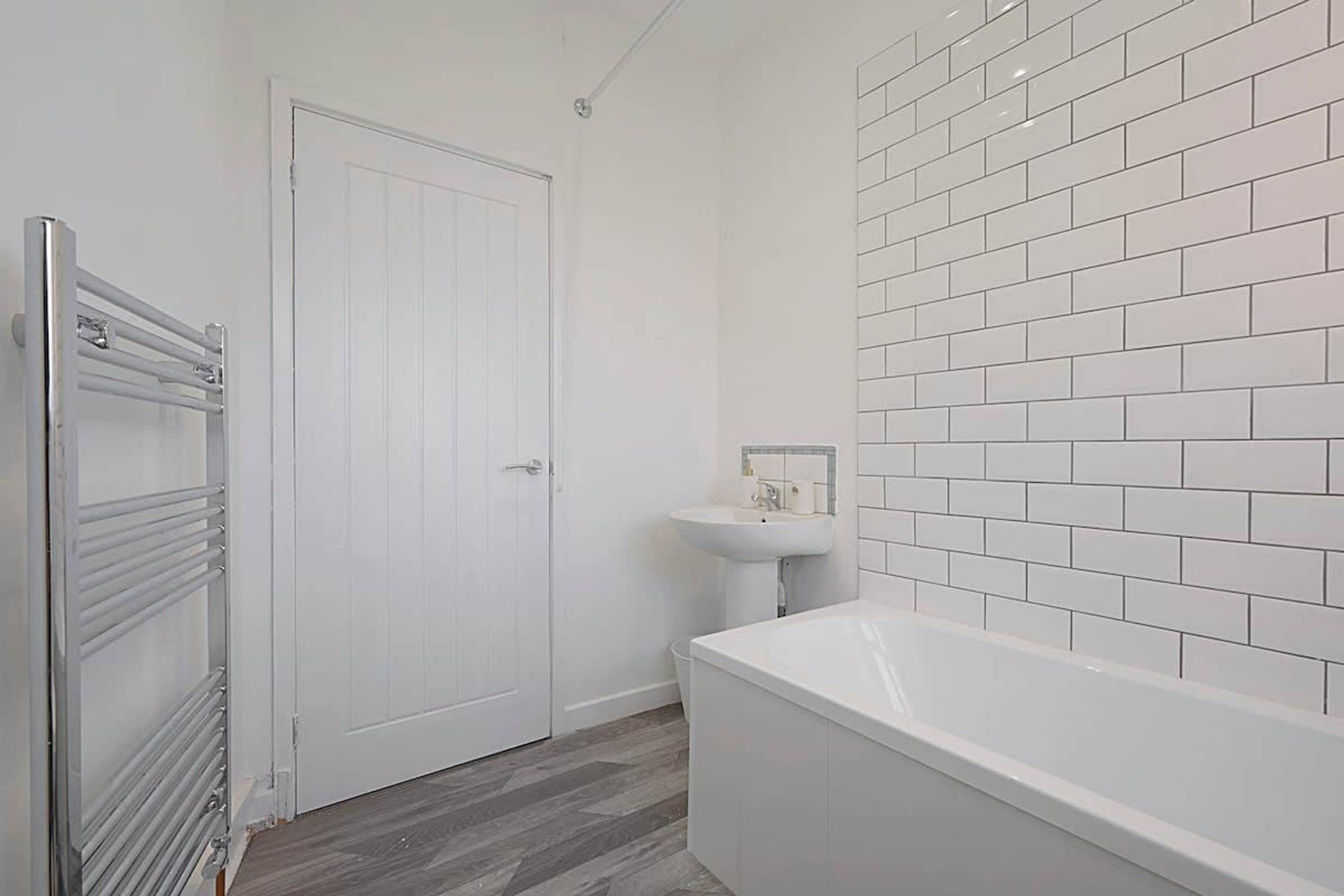 A bathroom with a white door, a white sink, and a white bathtub.